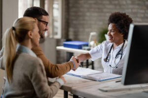 Imagem mostra médica em seu consultório apertando as mãos de dois empresários contábeis, para simbolizar como a equiparação hospitalar ajuda a reduzir a tributação