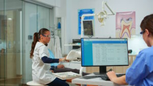 Imagem mostra dentista atendendo em clínica com computador em primeiro plano, para simular como funciona a equiparação hospitalar para dentistas e clínicas odontológicas